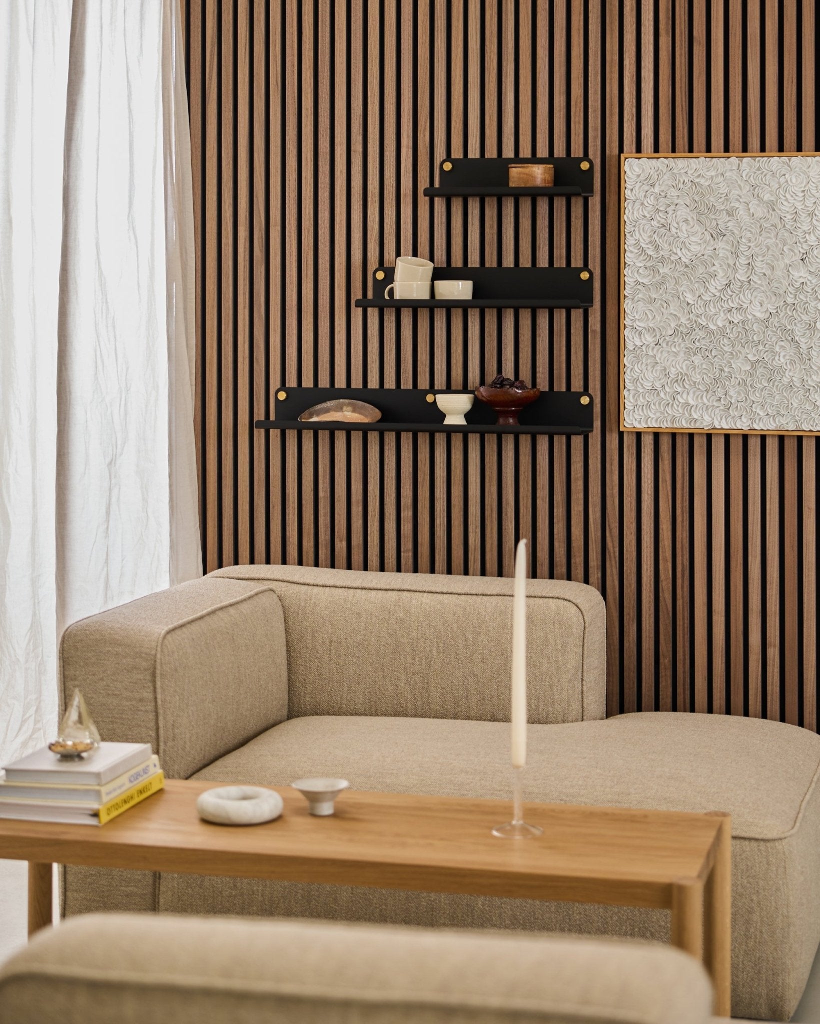 Soggiorno moderno con un divano beige, un tavolo in legno, una mensola larga WoodUpp black Norr (51,9 cm) e una parete Akupanel Pannello acustico materica con arte astratta.